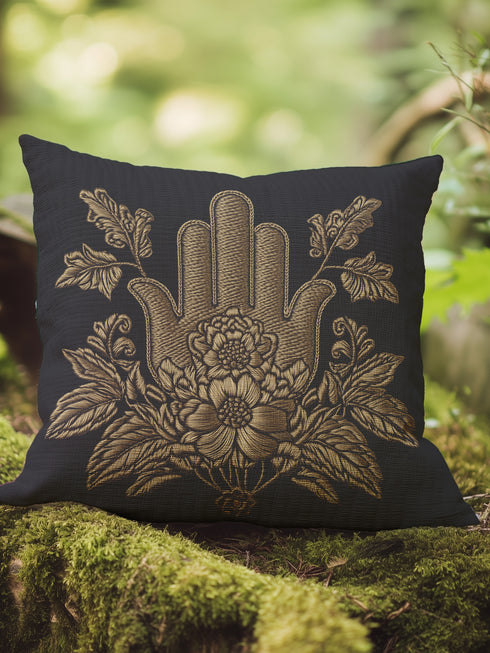 A black woven throw pillow featuring an embroidered gold Hamsa hand surrounded by intricate floral and botanical designs.